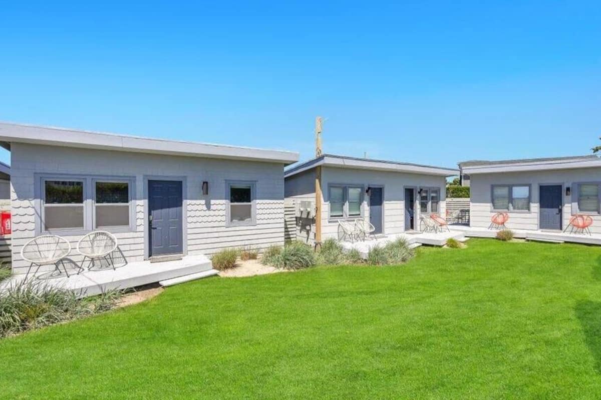 Une rangée de maisons mobiles à deux étages, avec une pelouse bien entretenue et un espace extérieur aménagé pour s’asseoir.