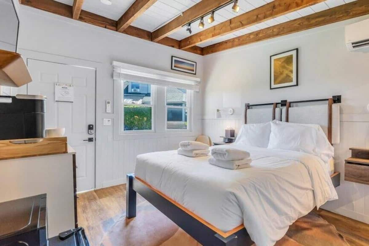 Une chambre à coucher comprenant un lit, des tables de chevet, une fenêtre, une porte et un téléviseur encastré.