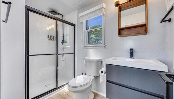 A modern bathroom with a glass shower enclosure, a toilet, and a sink with a mirror above it. - The Inn Spot (Hampton Bays)