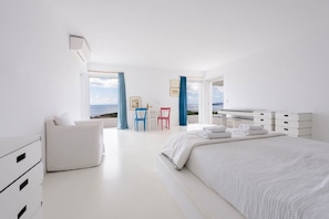 Ein modernes Schlafzimmer mit einem großen Bett, einem Schreibtisch und Blick auf das Meer.