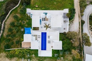 Ein modernes Haus mit einem zentralen, blauen Pool, umgeben von viel Grün und einer Steinmauer.