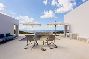 Eine Terrasse im Freien mit Tisch, Stühlen, zwei Sonnenschirmen, einer Couch und einer Bank.