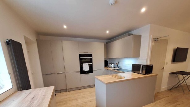 Una cocina moderna con una isla central, horno empotrado y un televisor de pantalla plana en la pared.