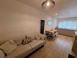 A modern living room with a sofa, a dining table, and a kitchen area.