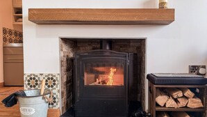 A wood-burning stove with a black front panel, a shelf above it, and a bucket of firewood to the left. - The Bothy in Fraserburgh (Fraserburgh)