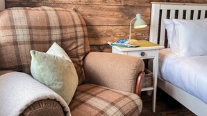 A bedroom with a plaid sofa, a bedside table with a lamp, a book, and a white bed. - The Bothy in Fraserburgh (Fraserburgh)