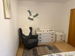 Et værelse med en sort lænestol, en hvid kommode med skuffer, et lille hvidt bord med håndvask og dekorativ vægkunst med tudser.