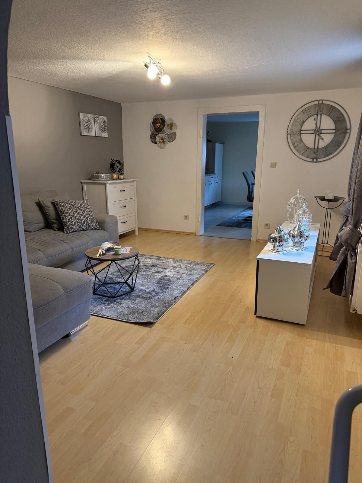 A living room with a grey sofa, a coffee table, a white cabinet, and a decorative wall clock.