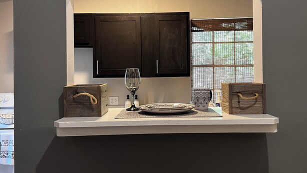Una cocina con armarios oscuros, una encimera blanca, una copa de vino y dos cajas de madera.