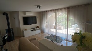 Uma sala de estar com sofá, mesa de vidro, televisão na parede e lareira.