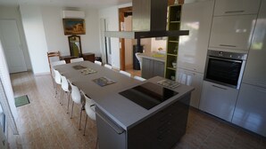Cozinha moderna com ilha central, eletrodomésticos de aço inoxidável e área de refeições com cadeiras.