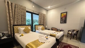 A hotel room with two beds, a desk, a chair, a small table, and a window with curtains. - Soaa Resort (Sirajganj)