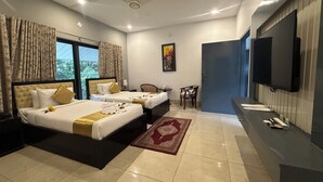 A hotel room with two beds, a TV, a desk, and a view of greenery outside. - Soaa Resort (Sirajganj)