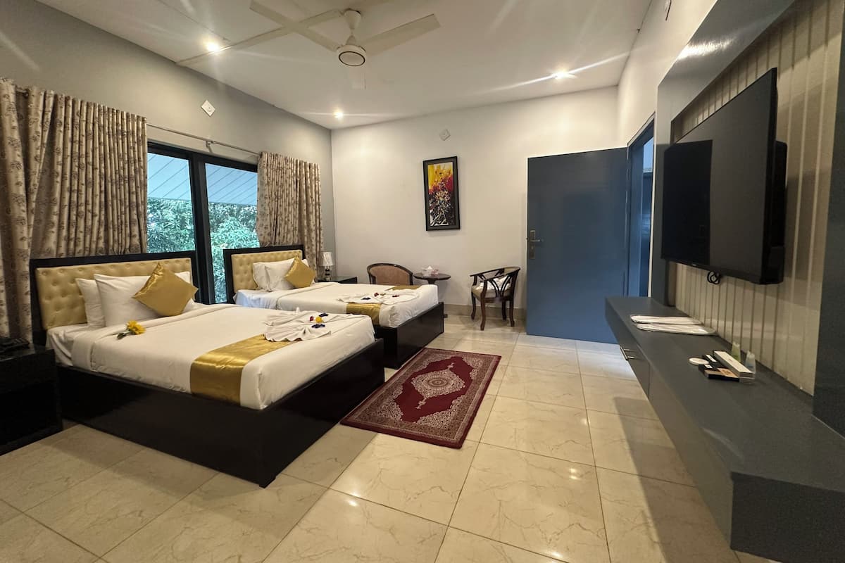 A hotel room with two beds, a TV, a desk, and a view of greenery outside.