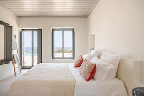 Ein Schlafzimmer mit Bett, Kissen, einer Leiter und Blick auf das Meer durch große Fenster.