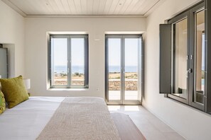 A bedroom with a bed, two large sliding doors, a view of the sea, and a wooden ceiling. - Amazing view of Naxos (X6W3+3G4 Paros, Greece)