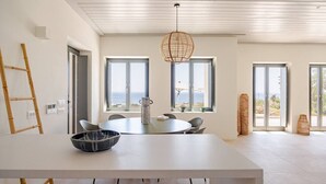 Ett modernt matområde med ett stort bord, stolar, en hängande lampa och stora fönster med utsikt över havet.