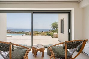 A balcony with a view of the sea, two wicker chairs, a small wooden table, and a sliding glass door. - Amazing view of Naxos (X6W3+3G4 Paros, Greece)