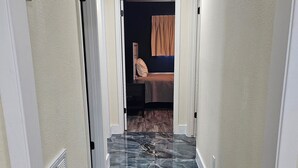 Un couloir au sol en marbre qui mène à une chambre à coucher, où se trouvent un lit et une table de chevet.