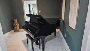 Un piano à queue se trouve dans un couloir, dont le sol est recouvert de marbre, et un vase est posé sur la gauche.