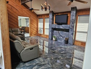 Een kamer met een open haard, een televisie erboven en een zithoek met een relaxfauteuil en een bank.