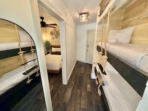 A room with bunk beds, a ceiling fan, a door, and a small plant. - Tybee Island Beachfront Condo, Pools, Dolphins, Ships (Tybee Island)