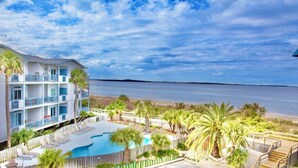 Een meerlaags hotel met een zwembad, uitzicht op het strand en palmbomen.