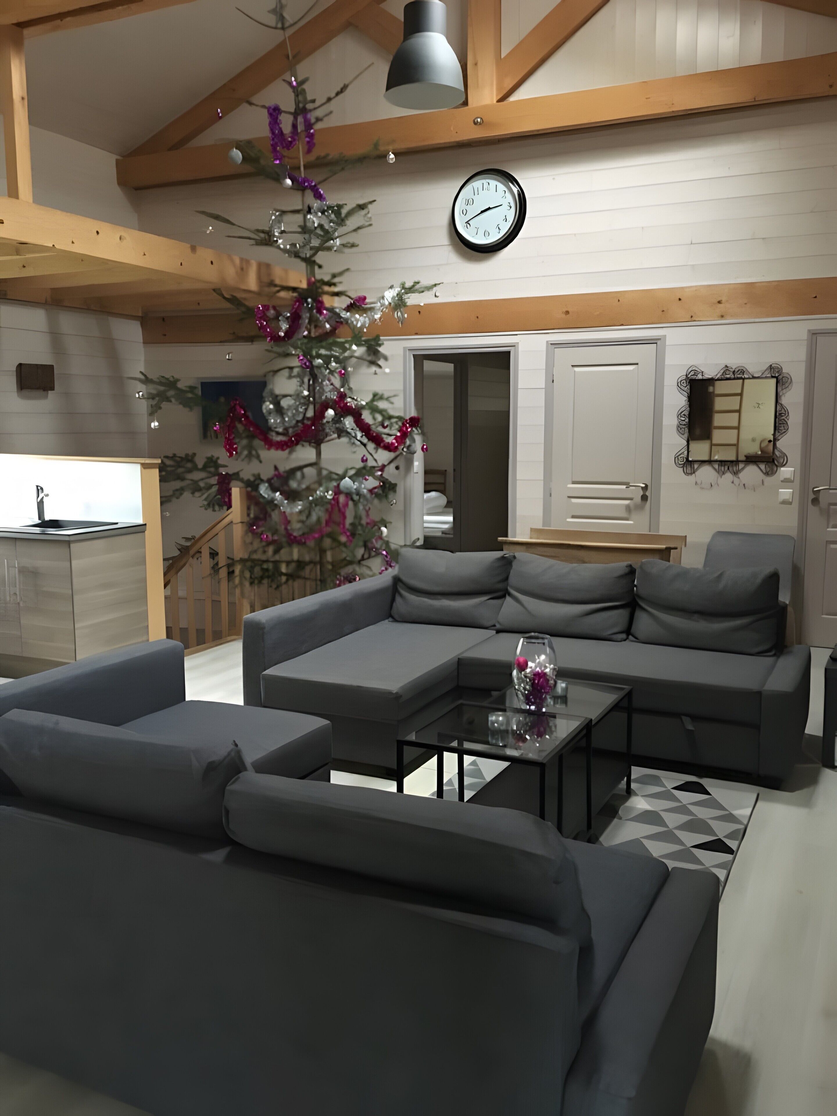 Una sala moderna con un sofá seccional, una mesa de centro, un reloj de pared y un árbol de Navidad decorado.