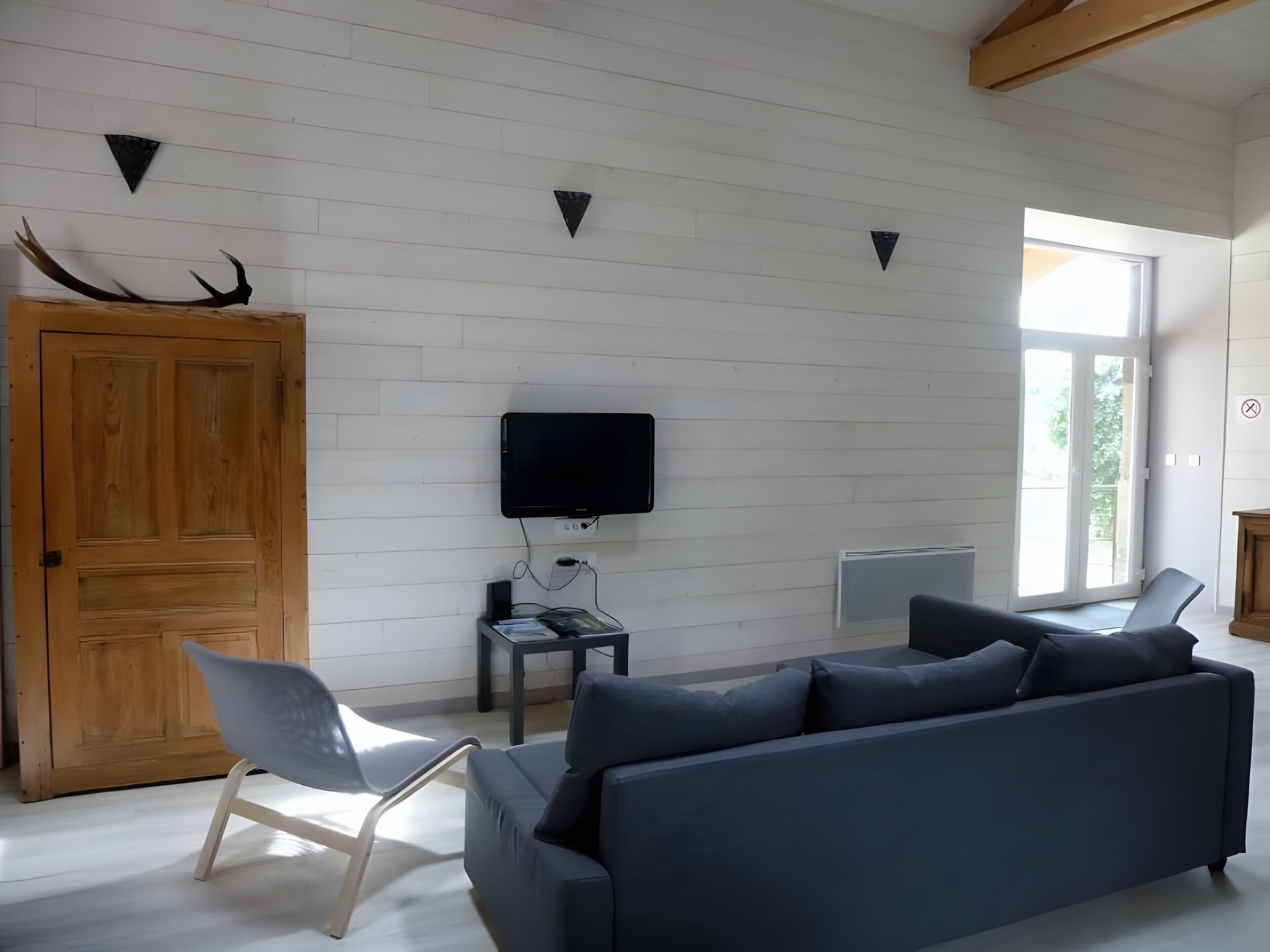 Un salon moderne avec une porte en bois, un téléviseur à écran plat, un canapé, un fauteuil et une fenêtre donnant sur un beau paysage.