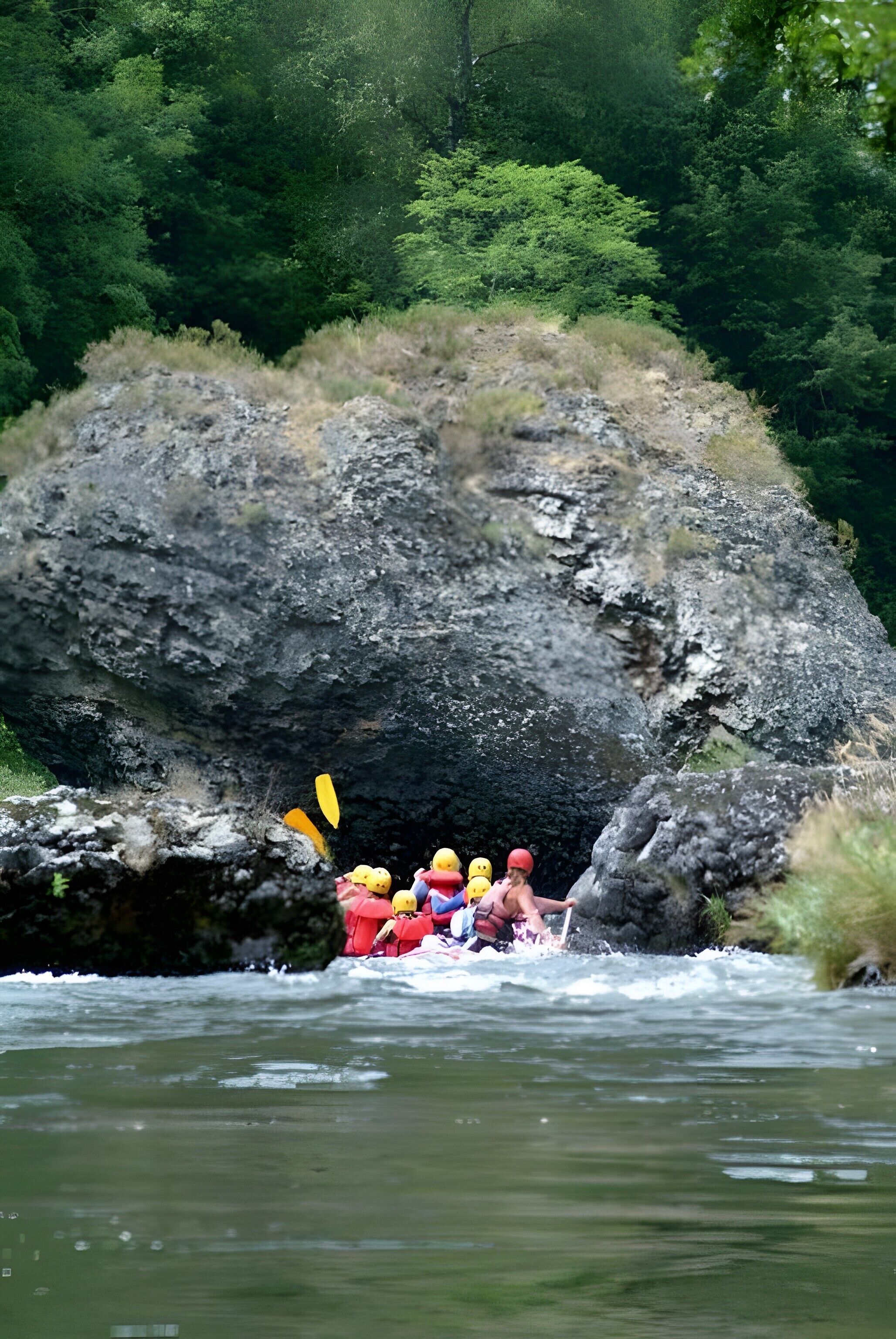 A group of people rafting through a river with a large rock formation in the background.