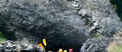 Un groupe de personnes fait du rafting sur une rivière, avec une grande formation rocheuse en arrière-plan.
