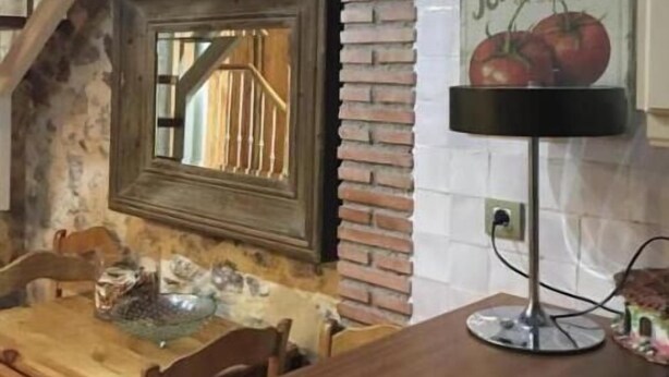 Un intérieur rustique avec des murs en briques apparentes, un escalier en bois, une table à manger en bois et un luminaire fixé au mur.