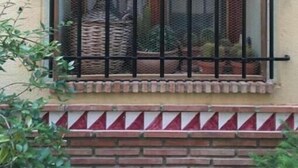 Une fenêtre avec des barreaux en métal, un petit élément décoratif au-dessus, et une base en briques.