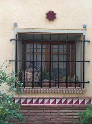 Ein Fenster mit Metallgitter, einem kleinen Ziertelement darüber und einem Ziegelunterbau.