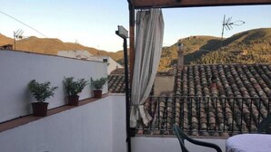 Un balcon donnant sur un paysage vallonné, un sol carrelé, une chaise et des plantes en pot.