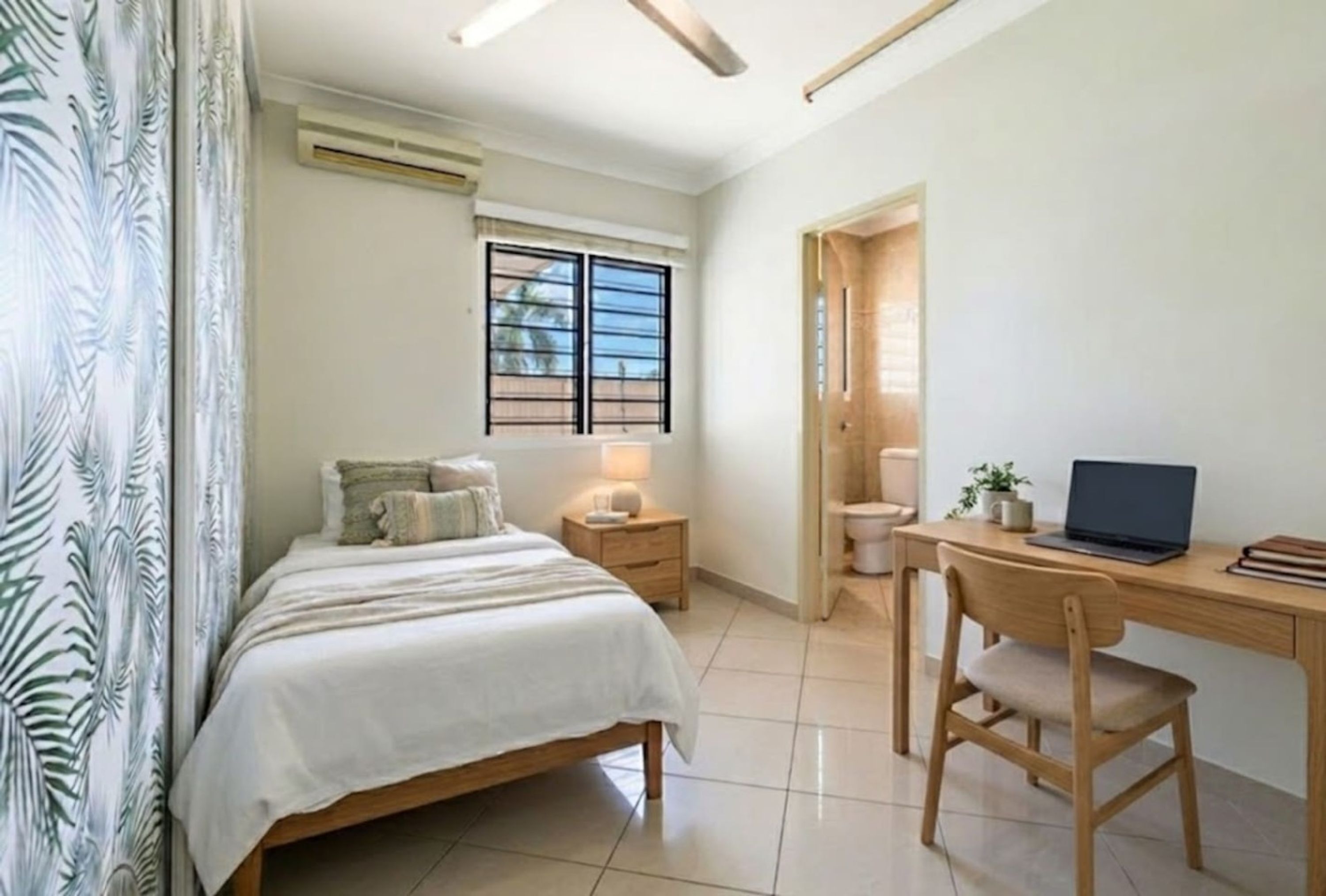 A bedroom with a bed, bedside table, lamp, and a desk with a chair.