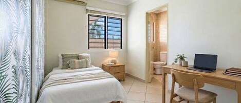 A bedroom with a bed, bedside table, lamp, and a desk with a chair.