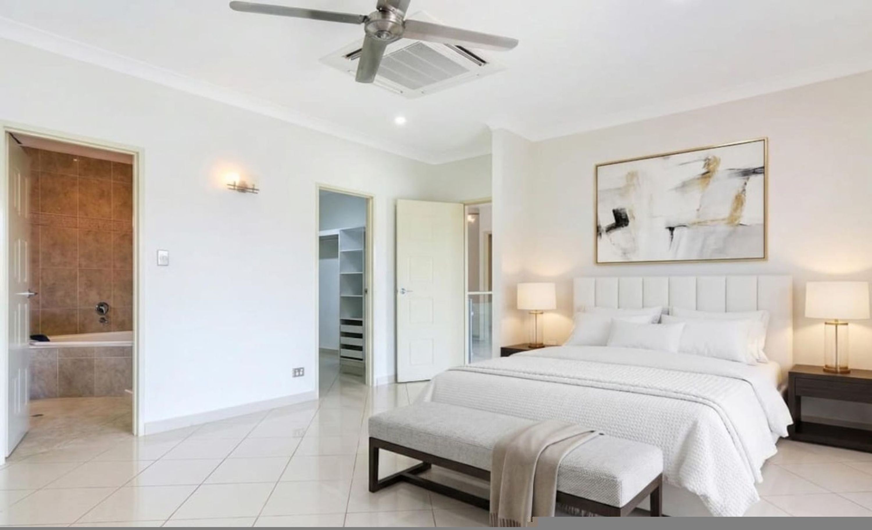 A bedroom with a bed, bedside lamps, a ceiling fan, a walk-in closet, and a bathroom with a shower.