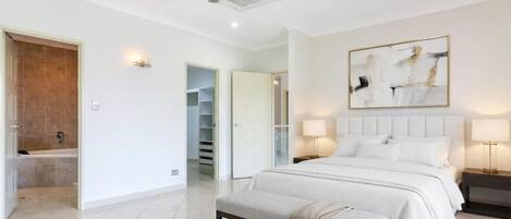 A bedroom with a bed, bedside lamps, a ceiling fan, a walk-in closet, and a bathroom with a shower.