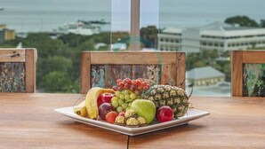 Une assiette de fruits est posée sur une table, avec en arrière-plan une étendue d’eau et des bâtiments.