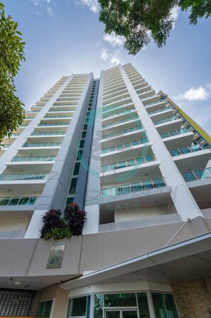 A high-rise building with multiple balconies, a clear sky, and a visible number '27' on the facade. - Coastal Magnificence Pool Workspace Parking (Darwin)