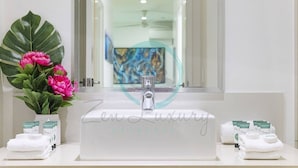 Une salle de bain moderne avec un grand miroir, un lavabo et une plante en pot ornée de fleurs roses.