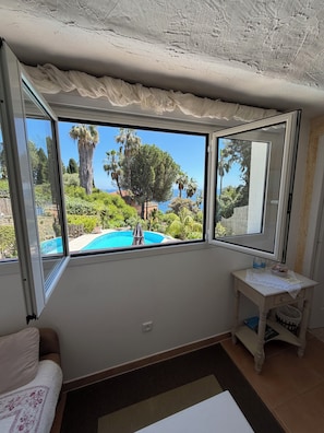 A room with a large window, a small table with a vase, and a chair. - Small villa close to the sea with swimming pool and garden of eden. holiday/reunion (Vallauris)