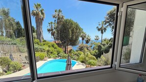 Una stanza con una grande finestra vista piscina e vegetazione lussureggiante.