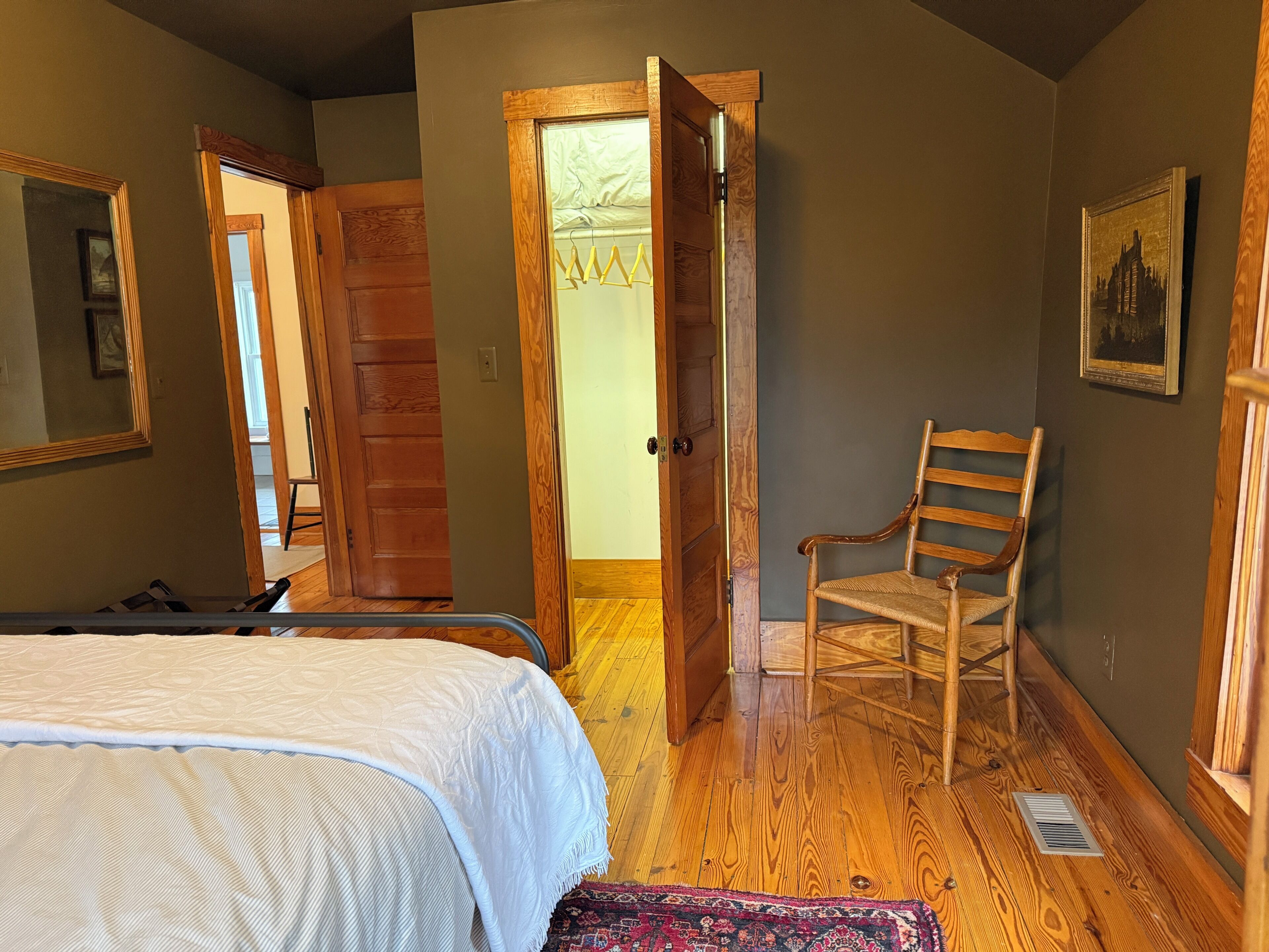 A bedroom with a bed, a chair, a wardrobe, and a door leading to another room.