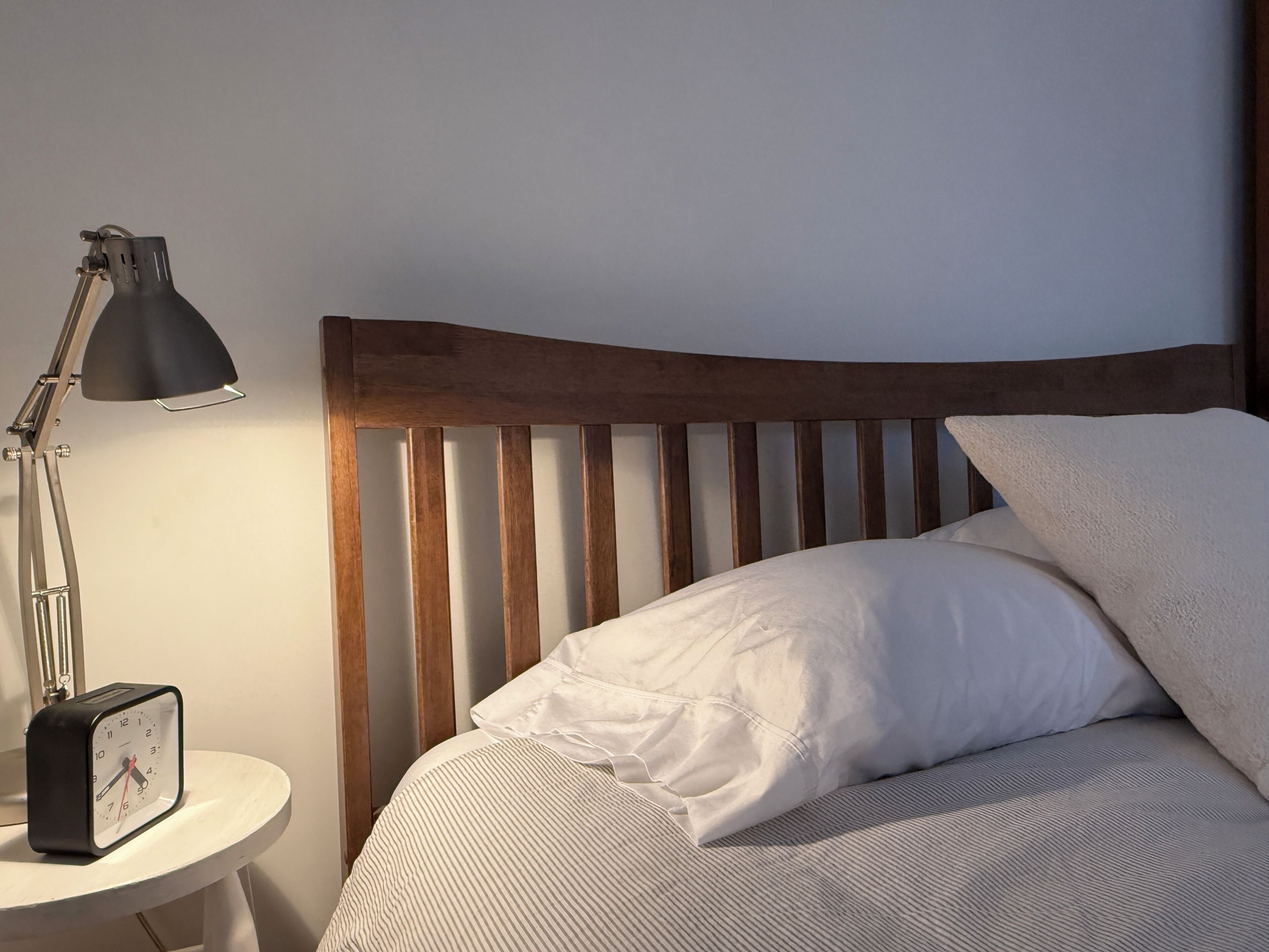 A bed with a wooden headboard, a bedside lamp, and a clock on a bedside table.