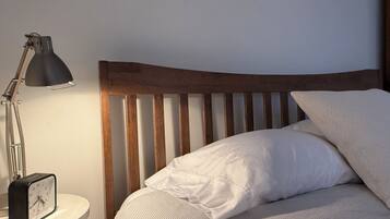 A bed with a wooden headboard, a bedside lamp, and a clock on a bedside table.