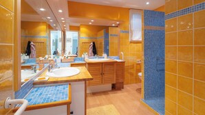 Ein modernes Badezimmer mit einem Holzbadezimmer-Möbel, einem großen Spiegel und einem Duschbereich mit blauen Fliesen.