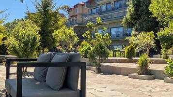An outdoor seating area with a sofa and a table, surrounded by trees and a building with multiple balconies.