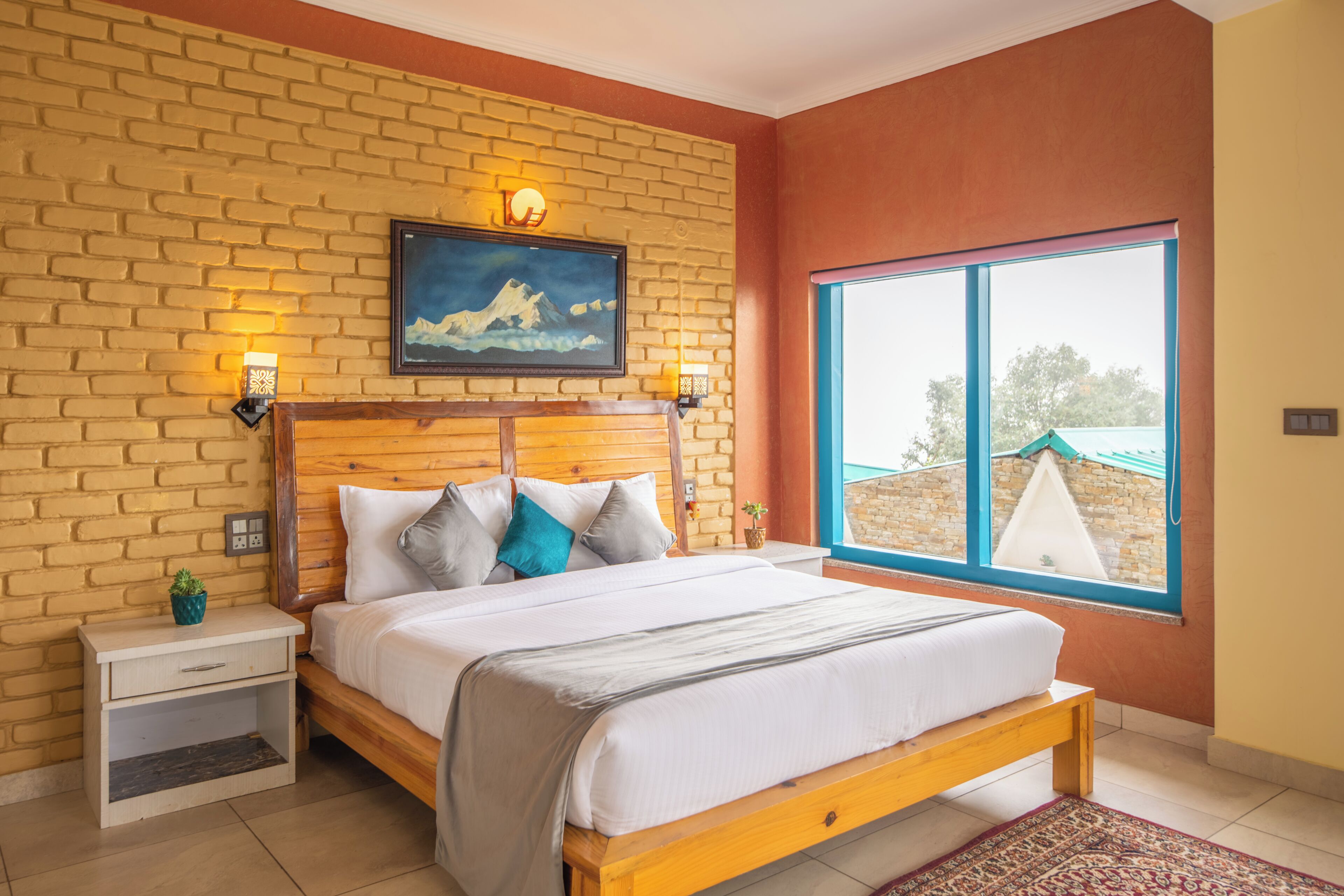 A bedroom with a brick wall, a wooden bed frame, a nightstand, a painting, and a window with a view.